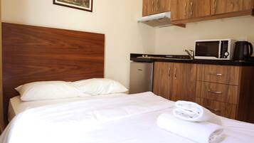 A hotel room with a bed, a wooden headboard, a microwave, a kettle, and a small refrigerator.