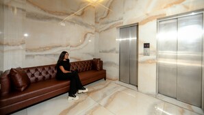A marble lobby with a brown leather sofa, an elevator, and a digital display. - Mar Mkhayel Studios (Beirut)