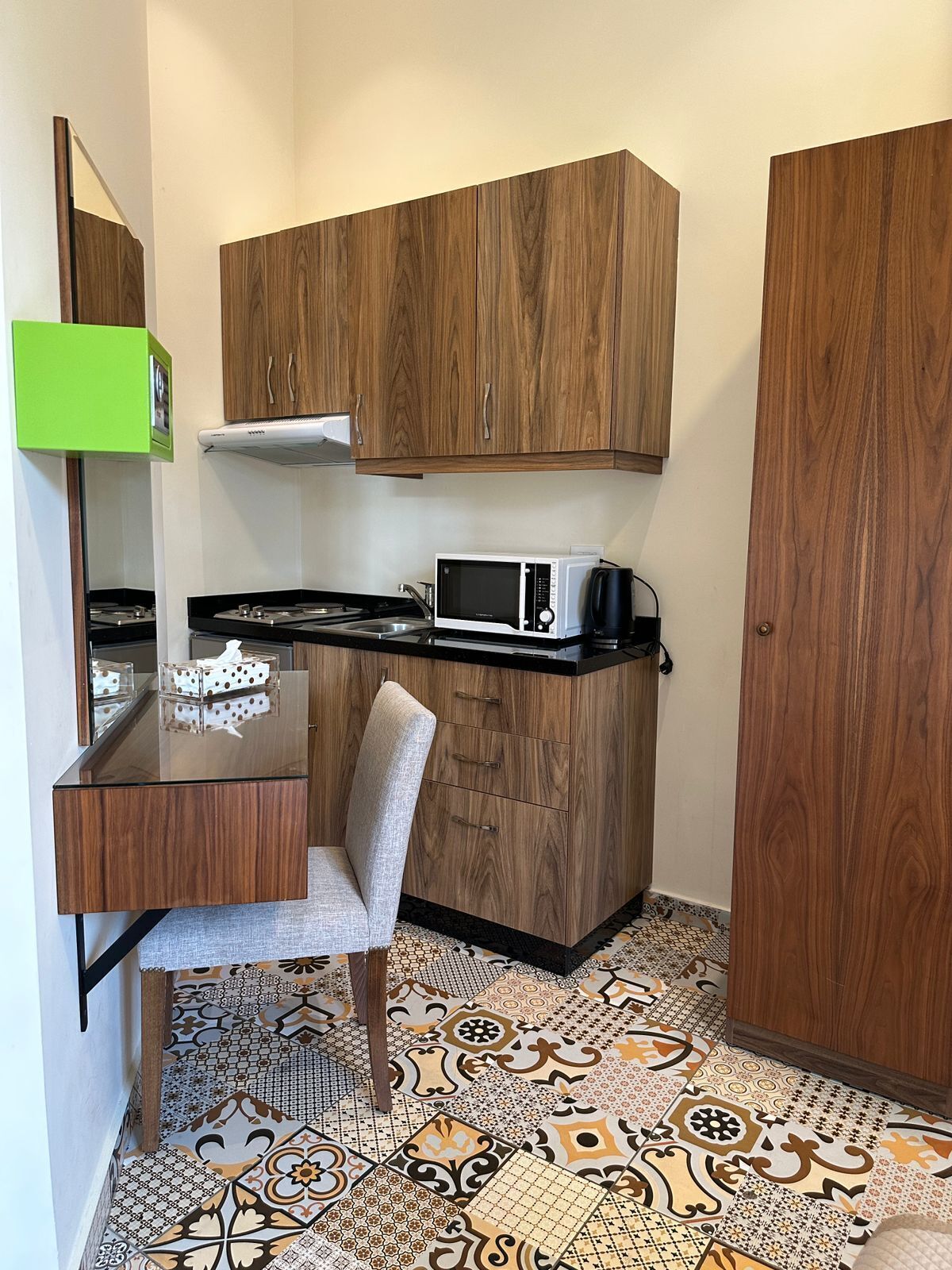 Una cucina compatta con mobili in legno, un forno a microonde, un fornello a gas e un pavimento decorato.