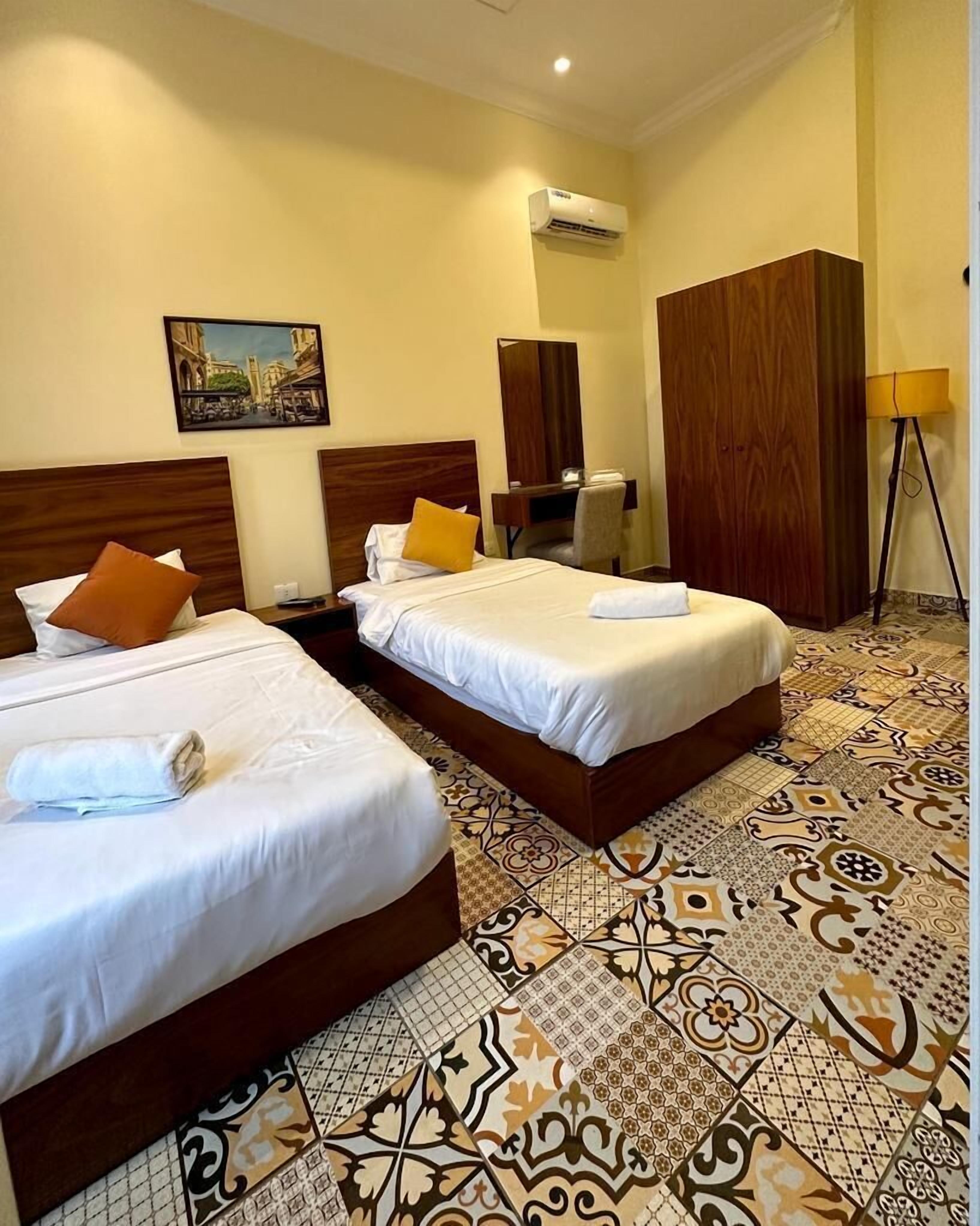 Habitación de hotel con dos camas, un escritorio, un armario y un cuadro en la pared.