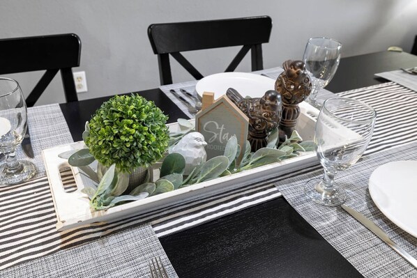 A dining table set with a tray containing a small potted plant, decorative items, and a sign.