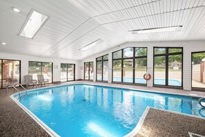 An indoor swimming pool with clear glass walls, a tiled floor, and a lifebuoy by the pool.