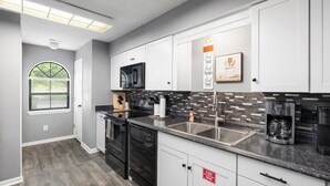 A modern kitchen with white cabinets, a black stove, and a stainless steel sink. - Spacious 2BR/2BA – Ground Level, Near Attractions (Branson)