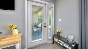 A room with a sliding glass door leading to a balcony, a small table with a vase of flowers, and a bookshelf with books and a basket. - Spacious 2BR/2BA – Ground Level, Near Attractions (Branson)