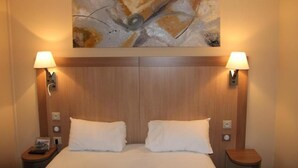 A hotel room with a wooden headboard, two bedside lamps, a painting above the bed, and a nightstand with a remote control. - Logis L'hôtel Restaurant Verrières (Verrieres-le-Buisson)
