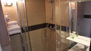 A glass-enclosed shower with a handheld showerhead, a glass door, and a white sink with a mirror. - Logis L'hôtel Restaurant Verrières (Verrieres-le-Buisson)