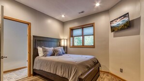 A bedroom with a bed, a window, a painting, and a door.