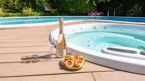 Un jacuzzi con un panel de control, una botella de champán y un plato de comida sobre una terraza de madera junto a una piscina.