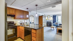 Eine moderne Küche mit Holzschränken, einem eingebauten Backofen und einem Geschirrspüler. Es gibt einen Essbereich mit einem blauen Sofa und einem Kamin.