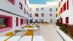 Un patio con mobiliario exterior y un edificio blanco con marcos de ventanas coloridos.