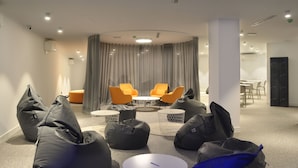 Una sala de conferencias moderna con mesas redondas, sillas naranjas y pufs negros.