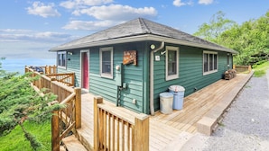 Een groen huis met een houten terras, een rode deur en een bord met de tekst 'Aan het meer'.