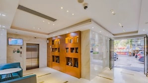 A hotel lobby with a reception desk, a seating area, a wooden display wall, an elevator, and a glass door leading outside. - City Comfort Inn (Guangzhou)
