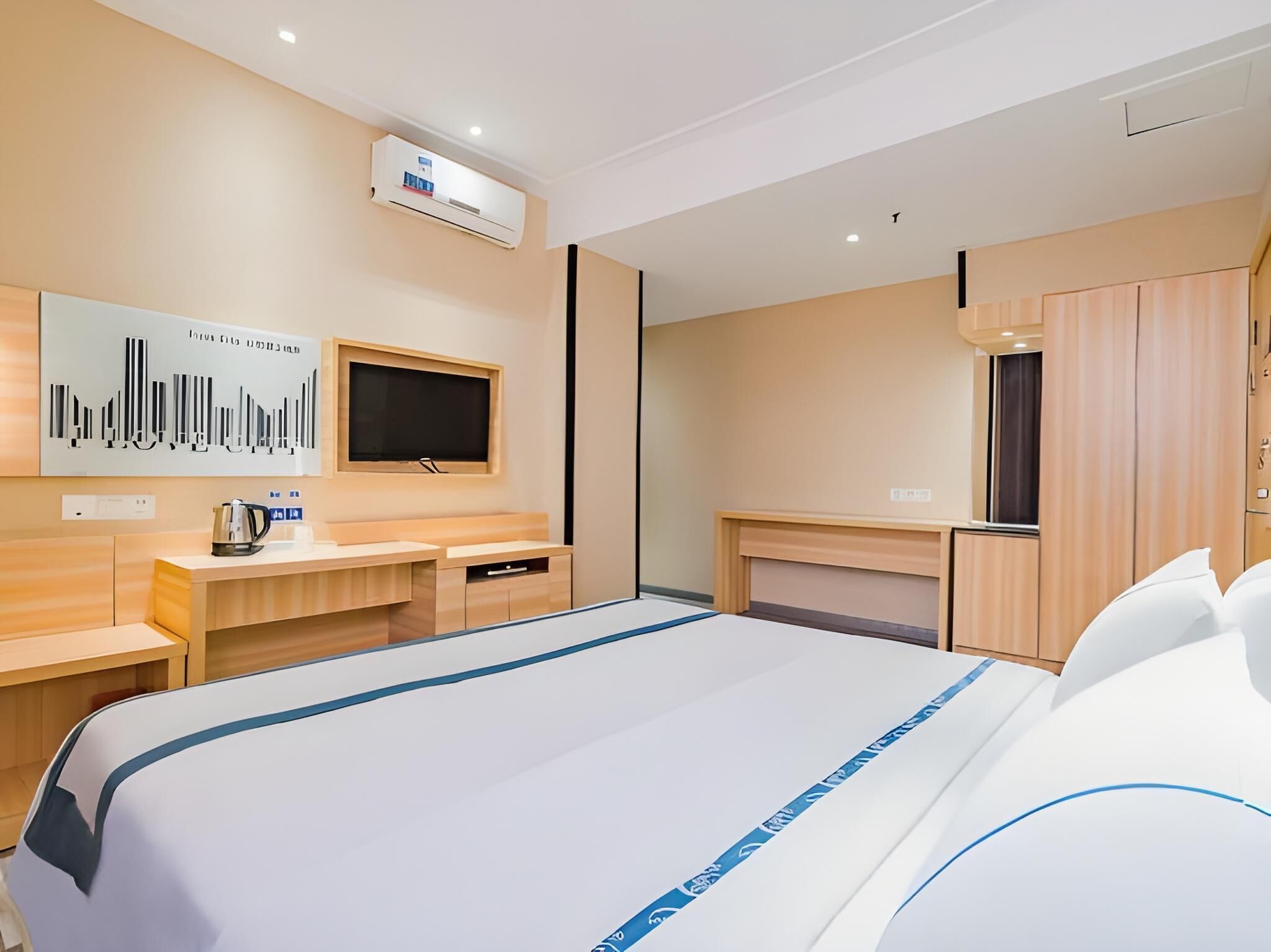 Ein modernes Hotelzimmer mit einem großen Bett, einem Schreibtisch mit Wasserkocher, einem Flachbildfernseher und einem Kleiderschrank.