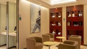 A lobby with seating, a painting of the Eiffel Tower, and a bookshelf with decorative items. - City Comfort Inn (Guangzhou)