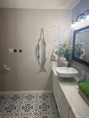 Ein Badezimmer mit einem weißen Waschbecken, einem Spiegel, einer Toilette und einem gemusterten Boden.