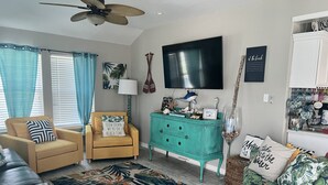 Un salon avec un fauteuil jaune, une commode turquoise, un canapé en cuir noir et un tapis à motifs.