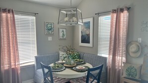 Un coin repas avec une table ronde, des chaises bleues et un lustre. Les murs sont ornés d’œuvres d’art encadrées, et un chapeau est posé sur un présentoir.