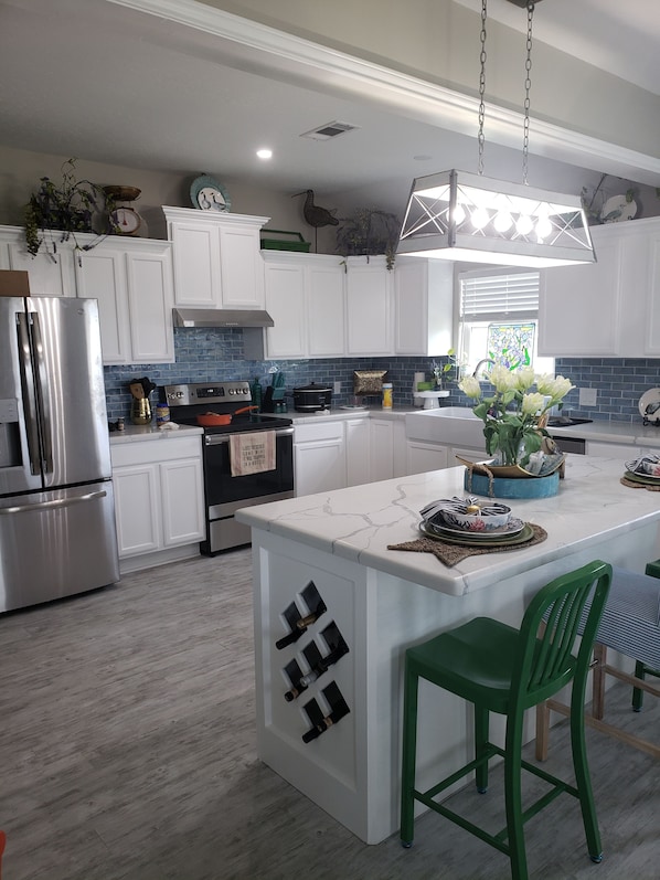 A modern kitchen with white cabinets, a central island, green bar stools, and a hanging light fixture. - Beach Access - Sleeps 8 - 3/2/Hot Tub (Crystal Beach)