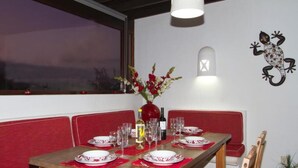 Un espace repas avec une table en bois dressée pour quatre personnes, des banquettes rouges rembourrées, un vase avec des fleurs et un luminaire fixé au mur.