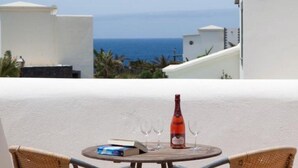 Un balcon donnant sur la mer, une bouteille de vin et deux verres sur une petite table.