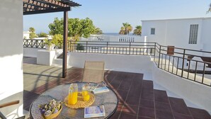 Eine Terrasse mit Glastisch, Korbstühlen und Blick aufs Meer.