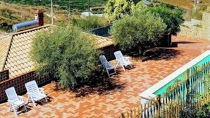 A rooftop terrace with lounge chairs, a pool, and a view of a coastal cityscape and mountains.