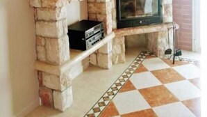 A living room with a brick wall, a flat-screen TV mounted above a stone fireplace, and a tiled floor.