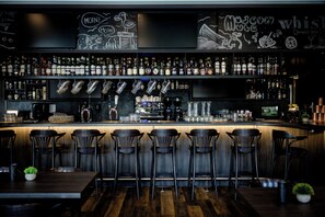Un bar con mostrador de madera, taburetes negros y una variedad de botellas de licor.