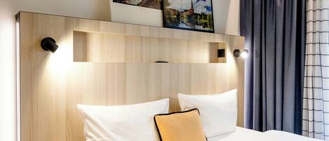 A hotel room with a wooden headboard, two white pillows, a single yellow pillow, and a bed with white bedding.