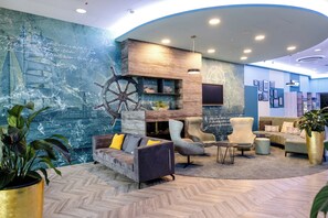 A modern lobby with a nautical mural, comfortable seating, and a large ship's wheel decoration.