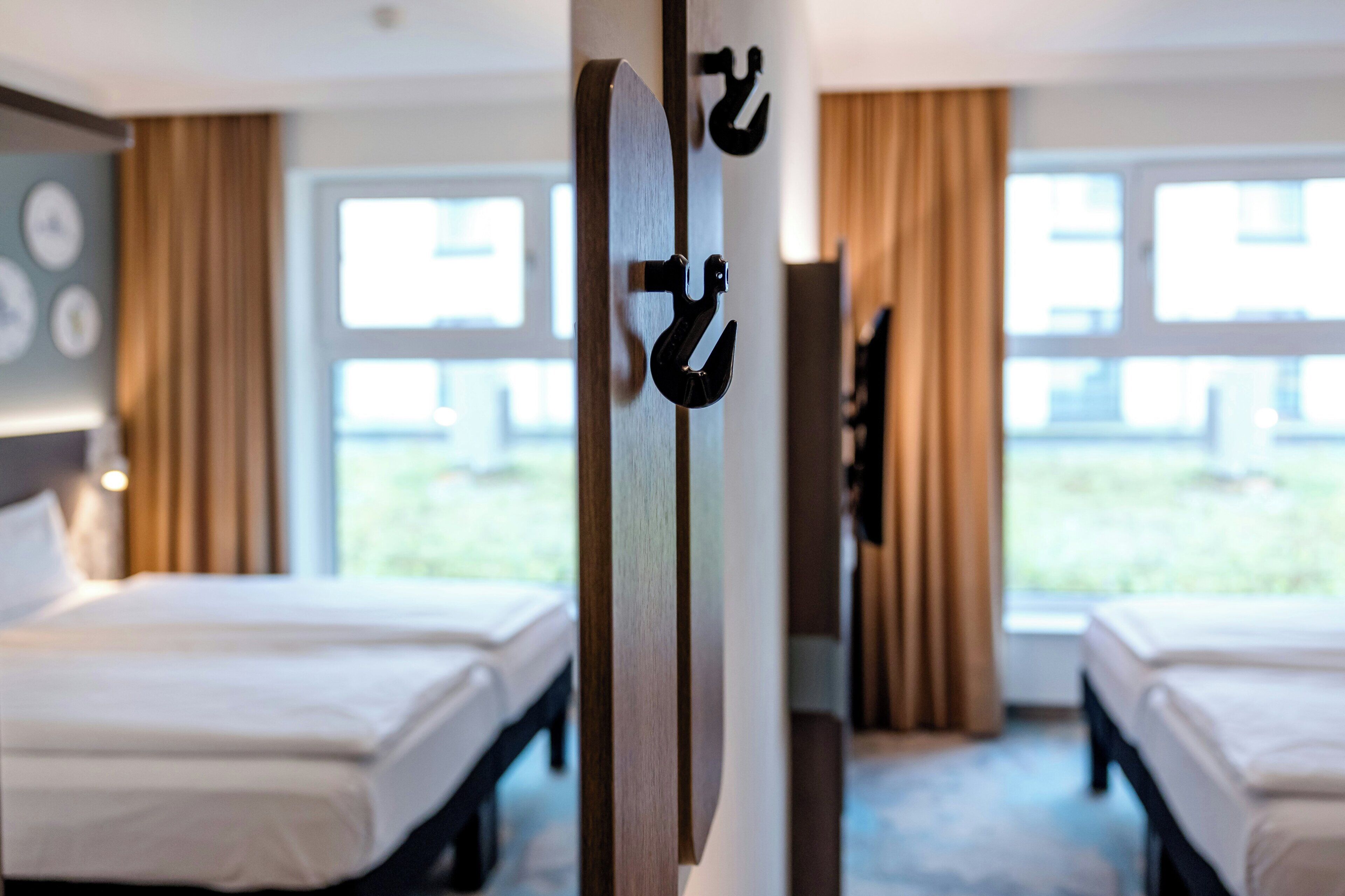 Habitación de hotel con dos camas, una puerta de madera con un perchero, y vistas al exterior a través de grandes ventanales.