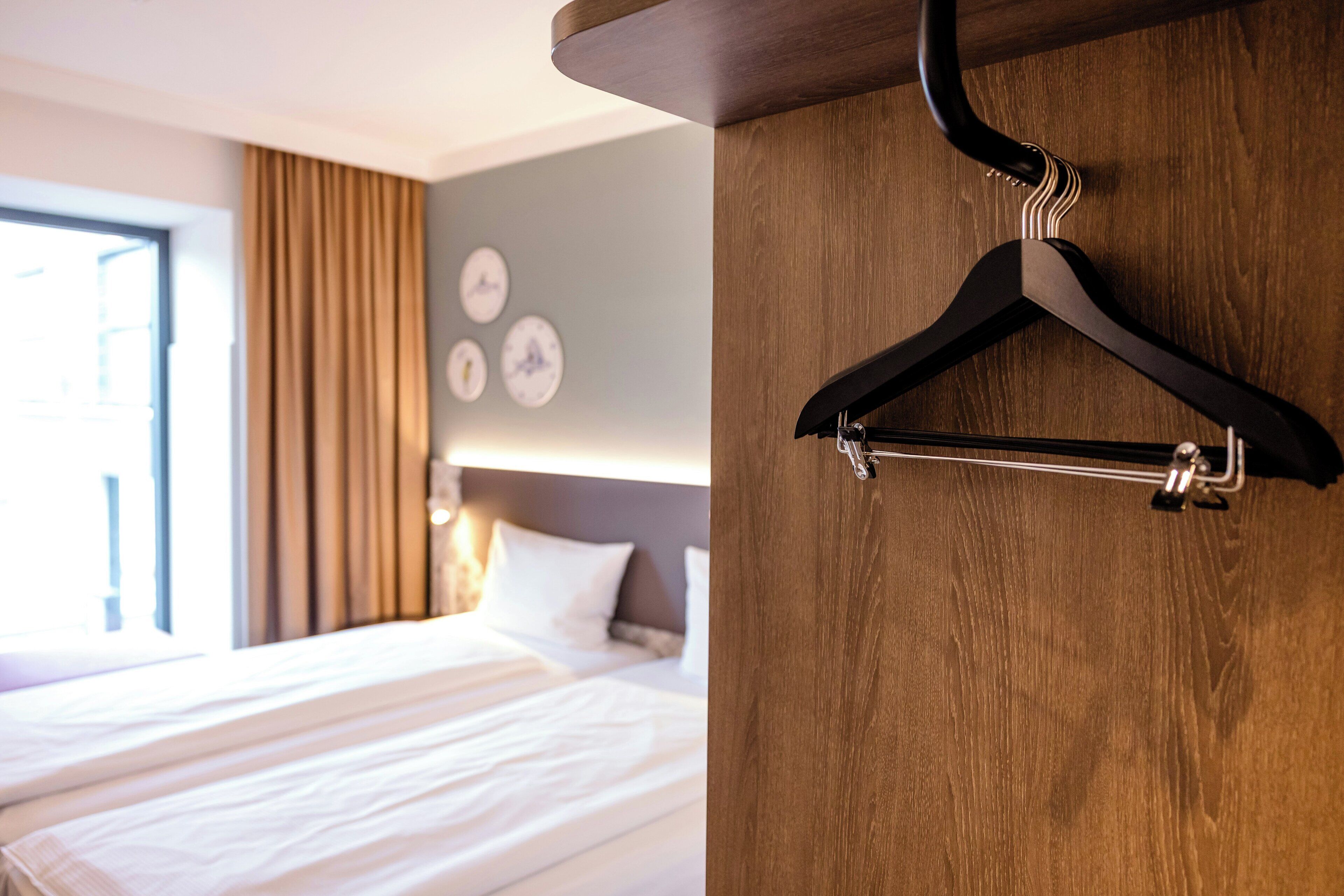 Une chambre d’hôtel avec un lit, une tête de lit en bois, un cintre noir et une horloge murale.