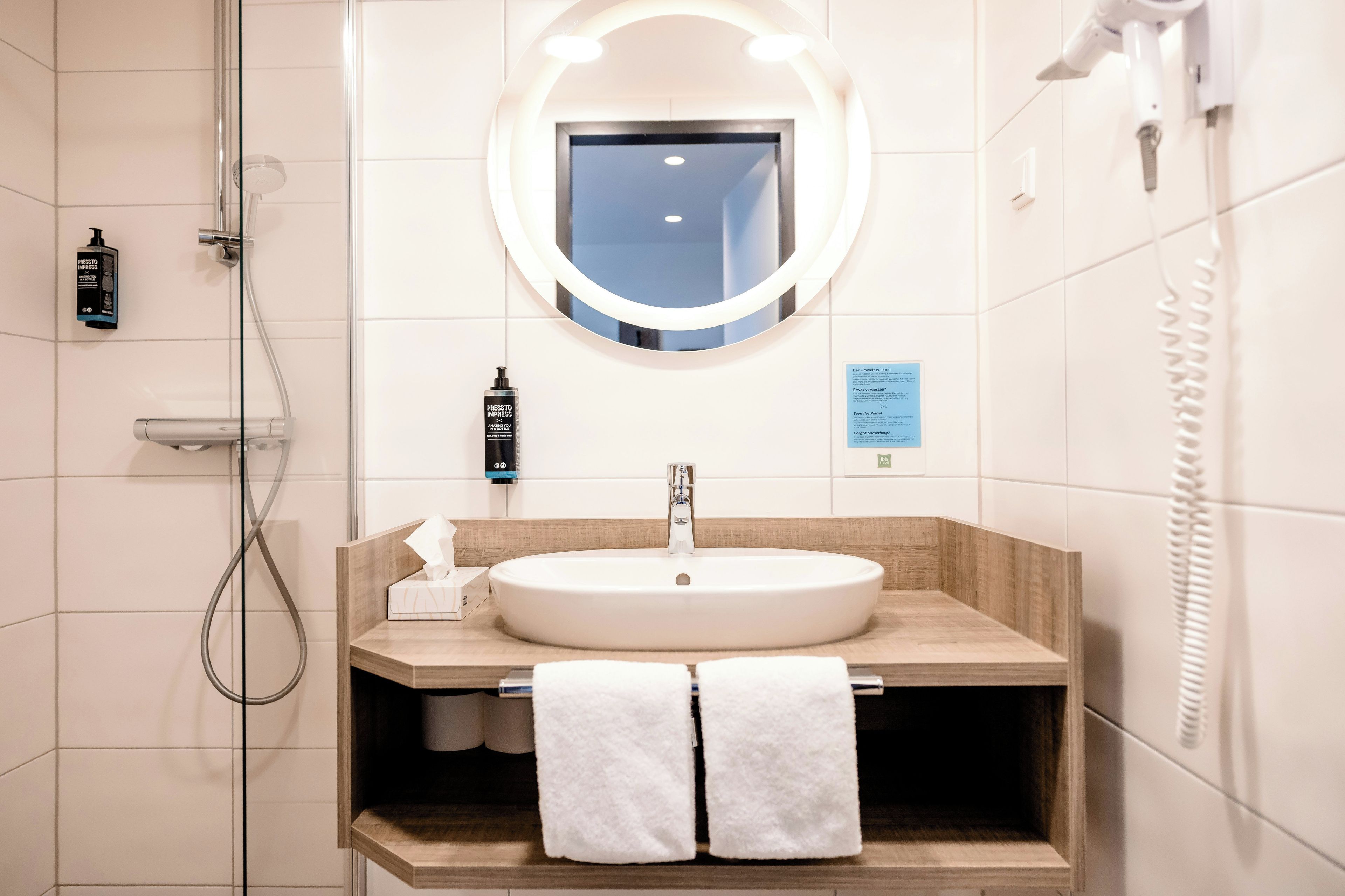 A bathroom with a round mirror, a sink, and a handheld showerhead.