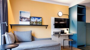 A modern living room with a sofa, a small table, a TV, and a kitchen area with a microwave. - Hotel Kiel-Schwedenkai (Kiel)