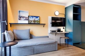 Un salon moderne comprenant un canapé, une petite table, un téléviseur et un coin cuisine avec un four à micro-ondes.