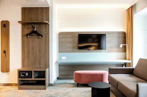 Una sala de estar moderna con un sofá, un otomán rosa, un televisor montado en una pared de madera y una mesita.