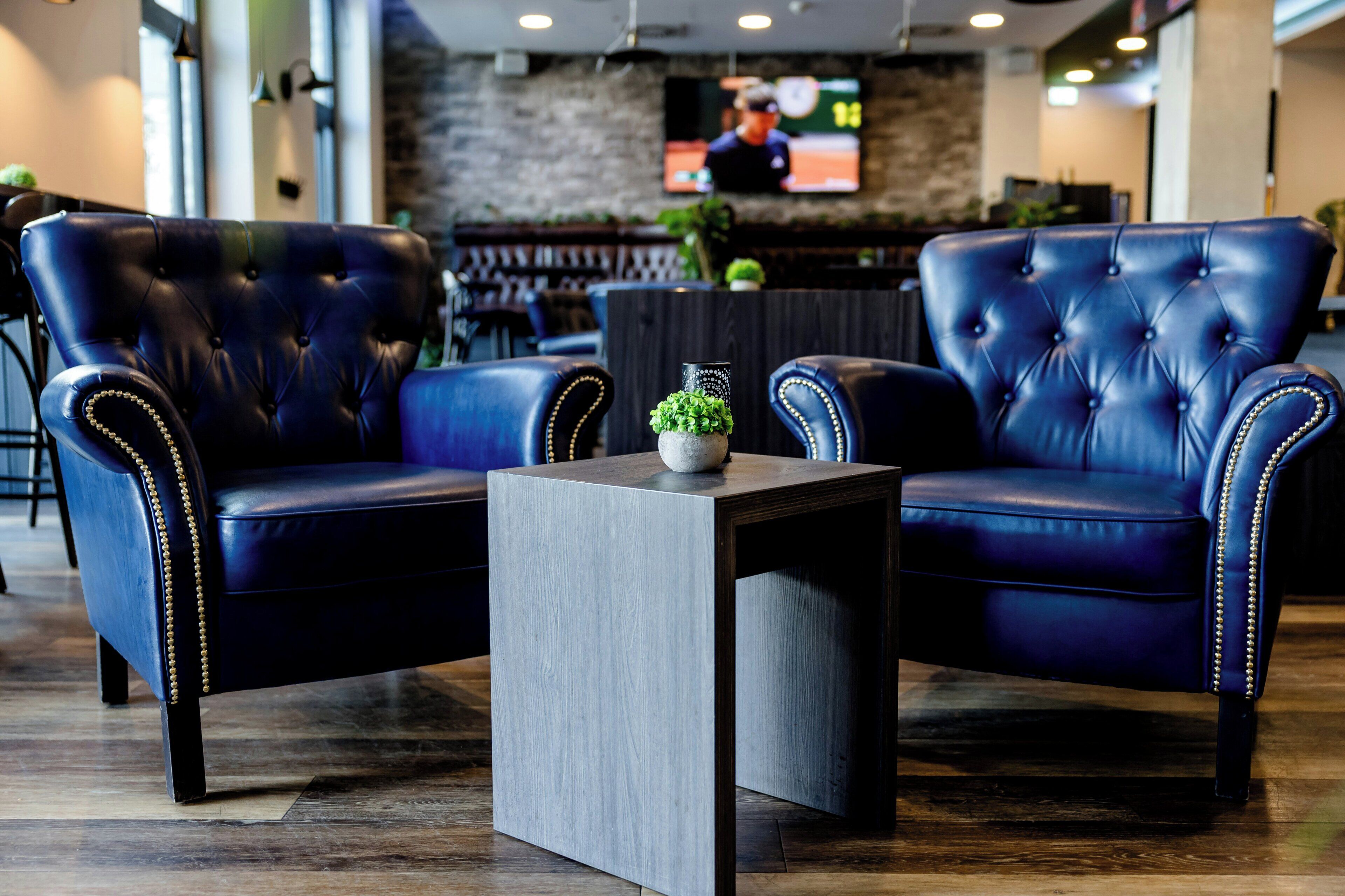 A seating area with two blue leather chairs, a small table with a plant, and a TV in the background.