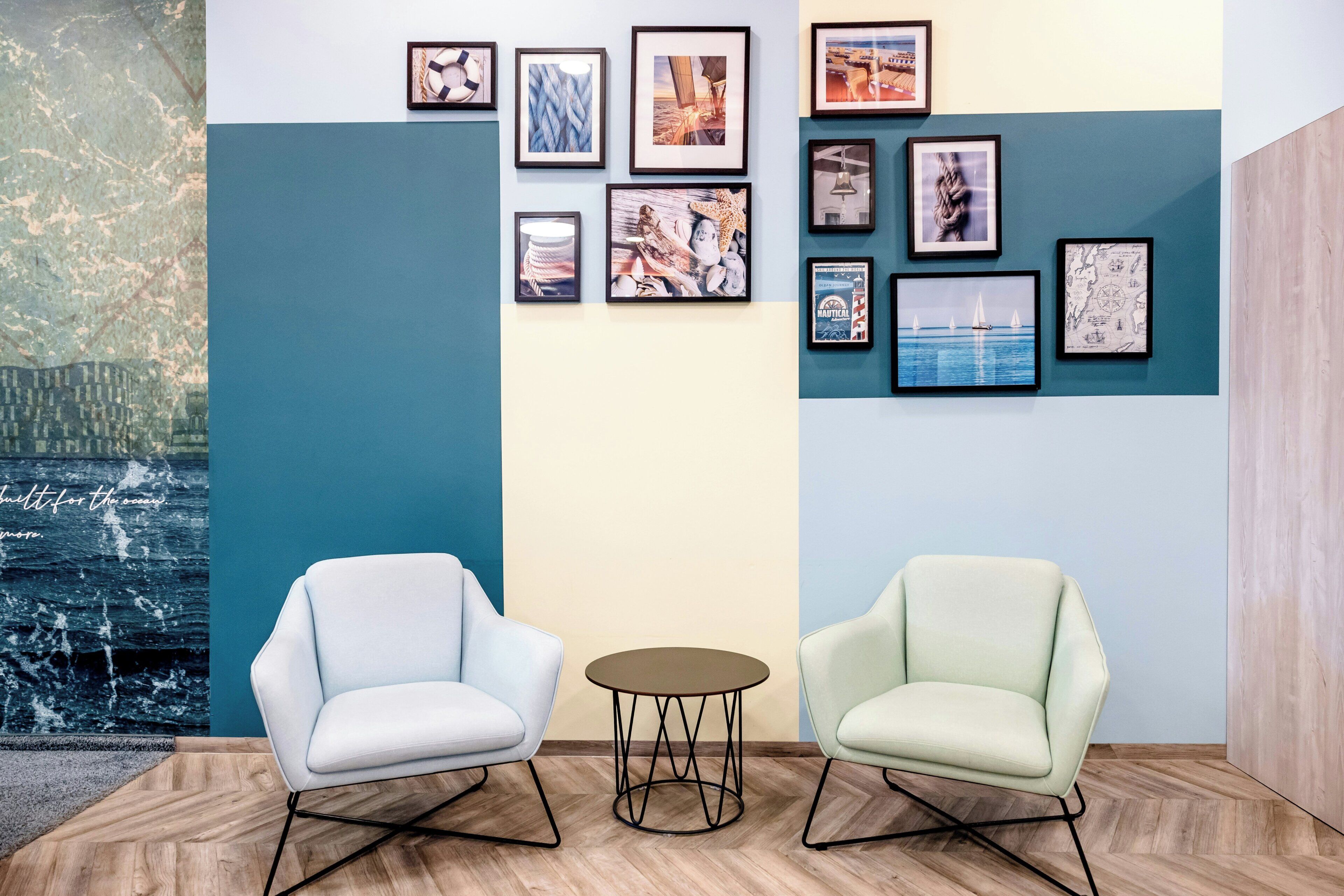 A room with two chairs, a small table, and a wall decorated with framed pictures.