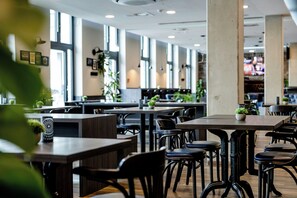 Un interior de restaurante moderno con techos altos, ventanas amplias y una mezcla de mobiliario de madera y metal.