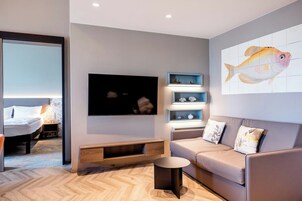 Una sala de estar moderna con un sofá, un televisor, una mesa de centro y una estantería de pared con objetos decorativos.
