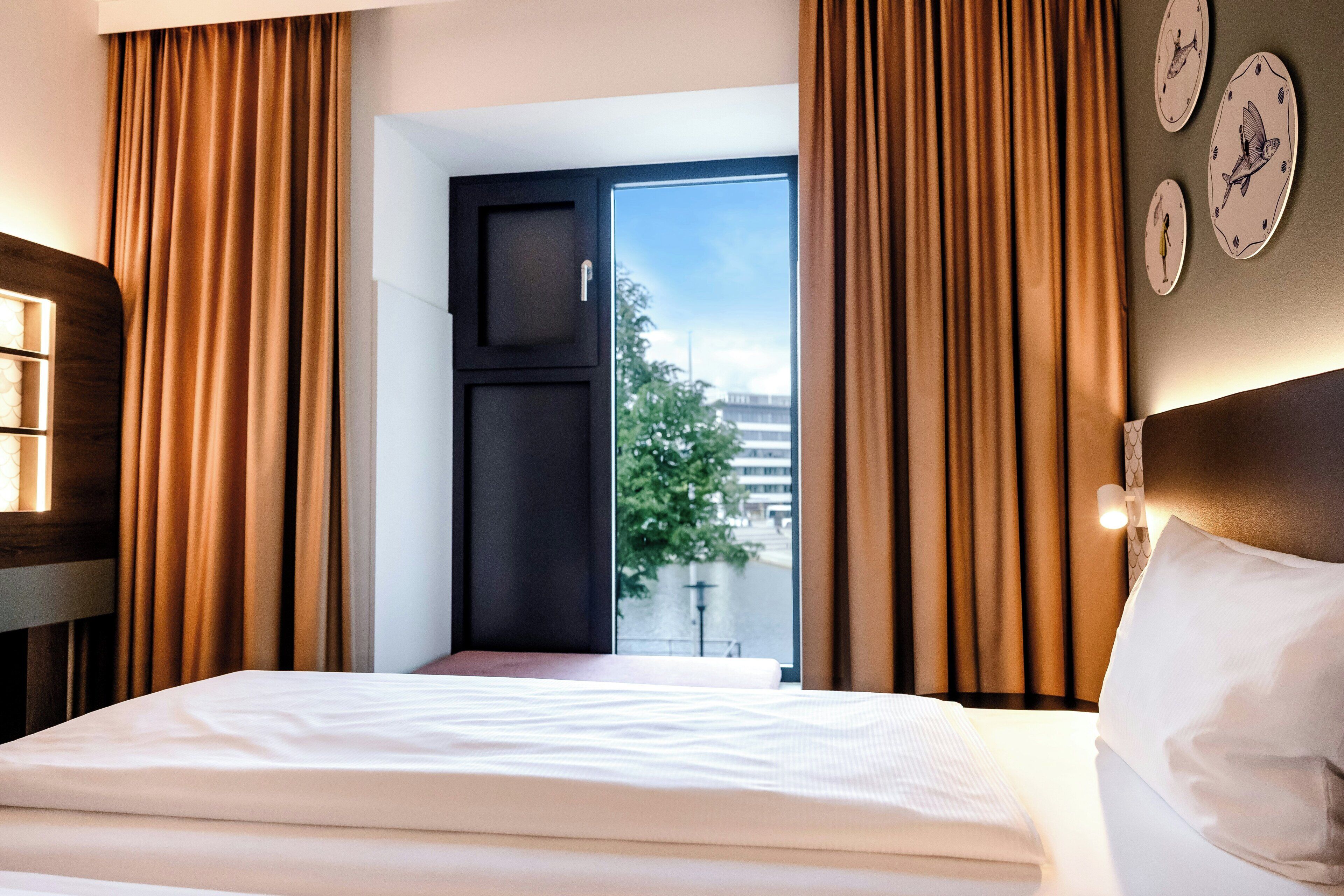 Habitación de hotel con cama, cortinas, ventana y relojes de pared.