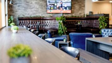 Zona de bar con asientos, un televisor montado en la pared y plantas en macetas.