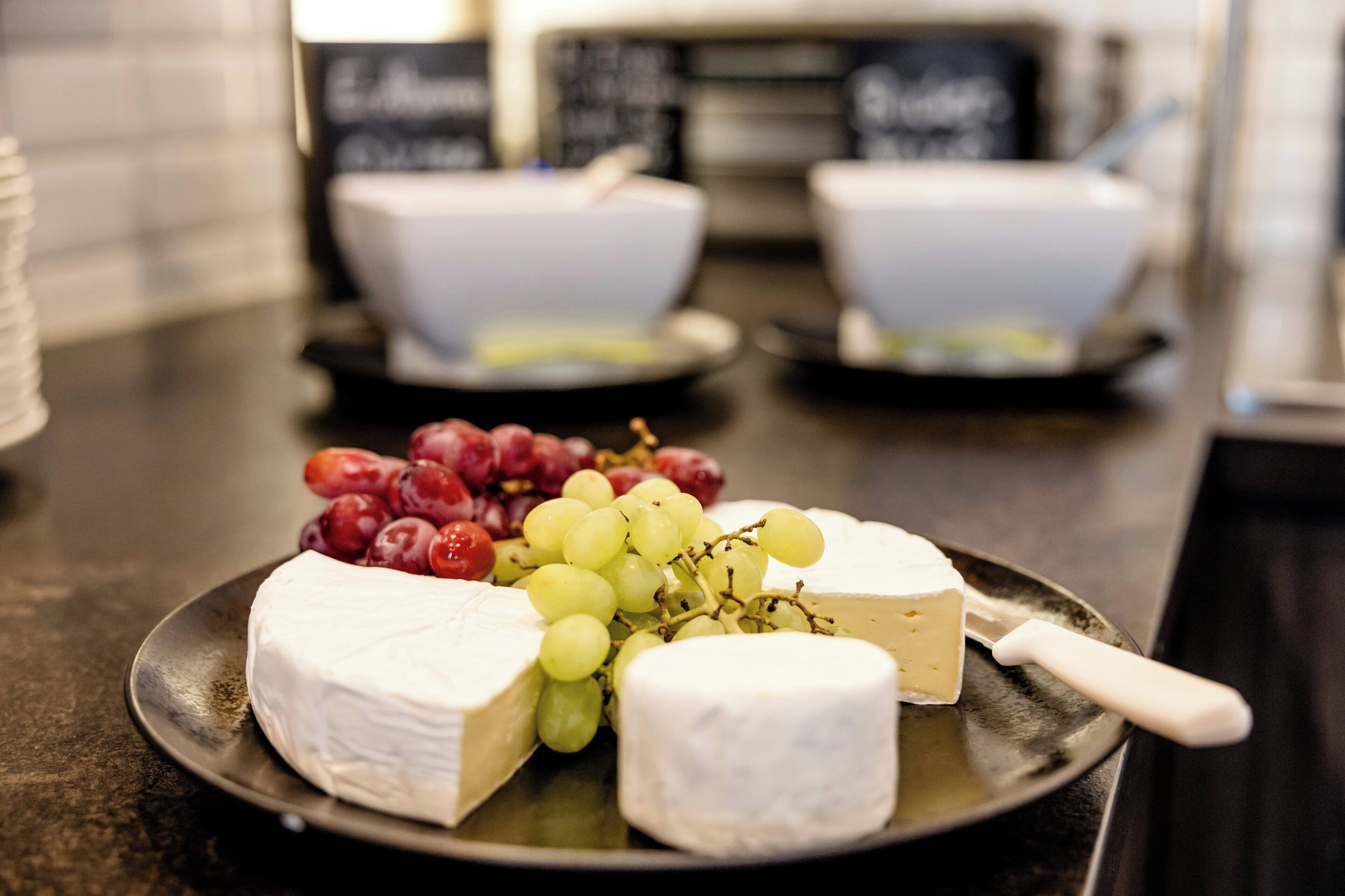 Un plato de queso y uvas sobre una mesa, con cuencos al fondo.