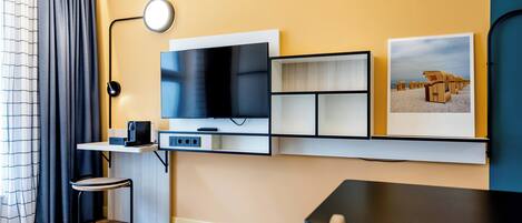 Una sala moderna con un televisor de pantalla plana, una mesita, una silla y un estante en la pared.