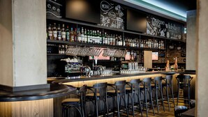 A bar area with multiple stools, shelves with bottles, and a counter. - Hotel Kiel-Schwedenkai (Kiel)