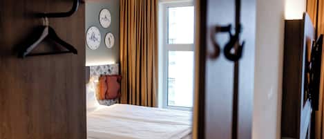 A hotel room with a bed, a wardrobe, a mirror, and a window with curtains.