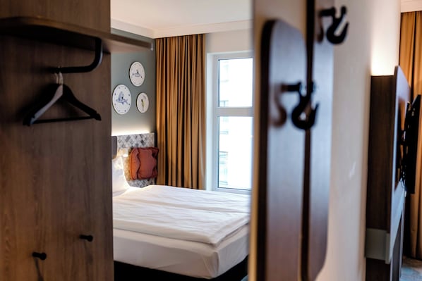 A hotel room with a bed, a wardrobe, a mirror, and a window with curtains. - Hotel Kiel-Schwedenkai (Kiel)