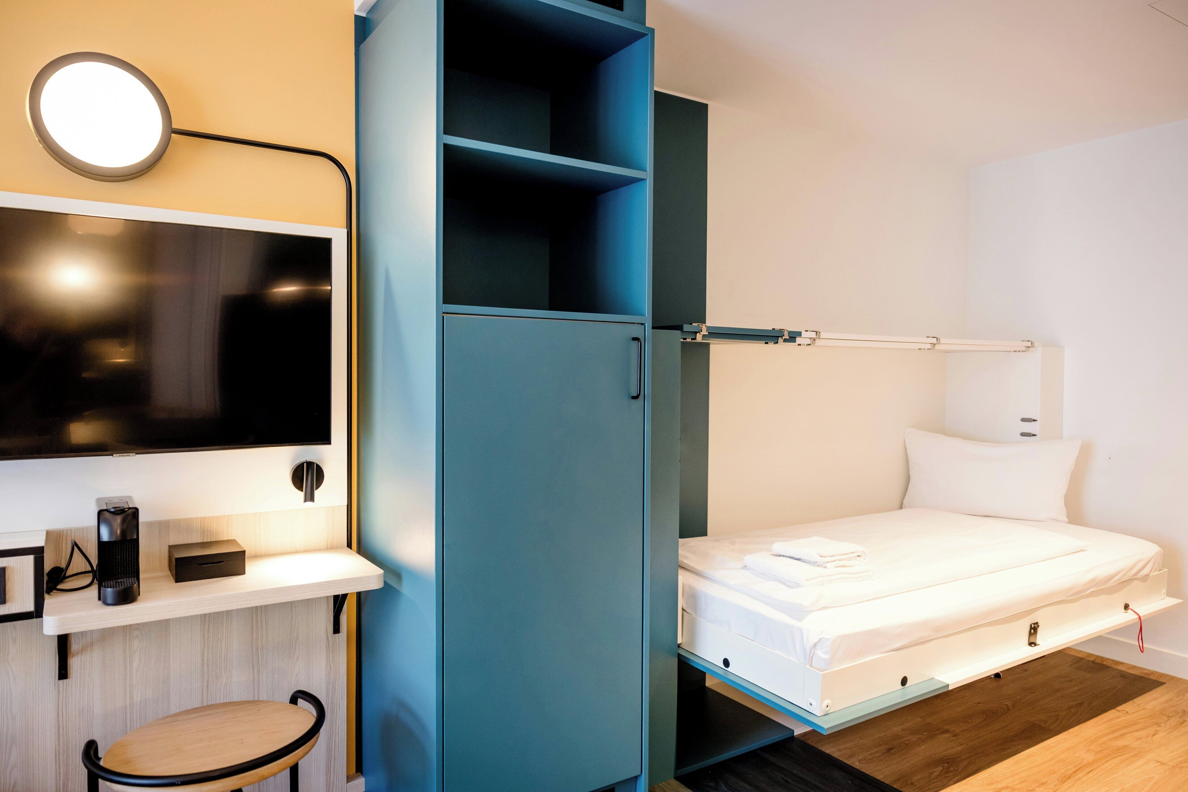 Habitación compacta con cama, escritorio con computadora, silla, armario y televisor.