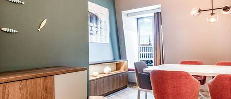 Een moderne eetruimte met een witte tafel en rode stoelen, een houten kast en een wand met decoratieve vissen.